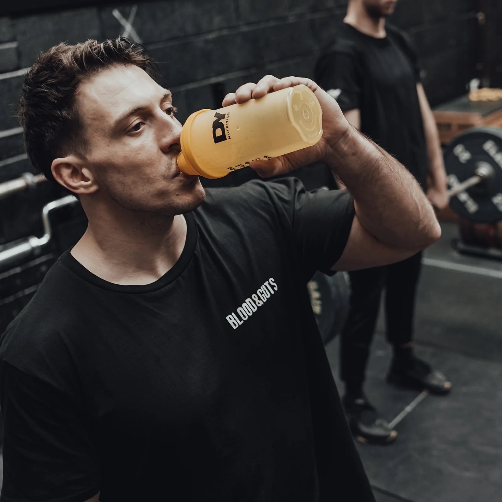 Person i svart T-shirt som dricker ur gul dryckesflaska med lock