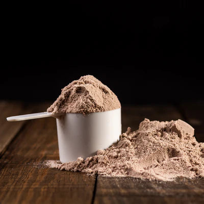 Skopa med chokladfärgat proteinpulver och vit burk, med högen i förgrunden